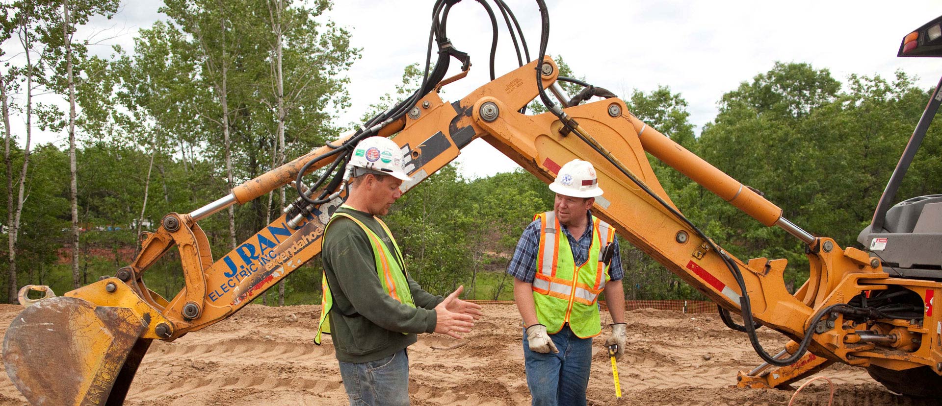 Construction worksers discuss plan for work in front of excavator arm